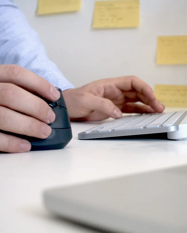 Hände an Tastatur und Maus an einem Schreibtisch mit Notizzetteln